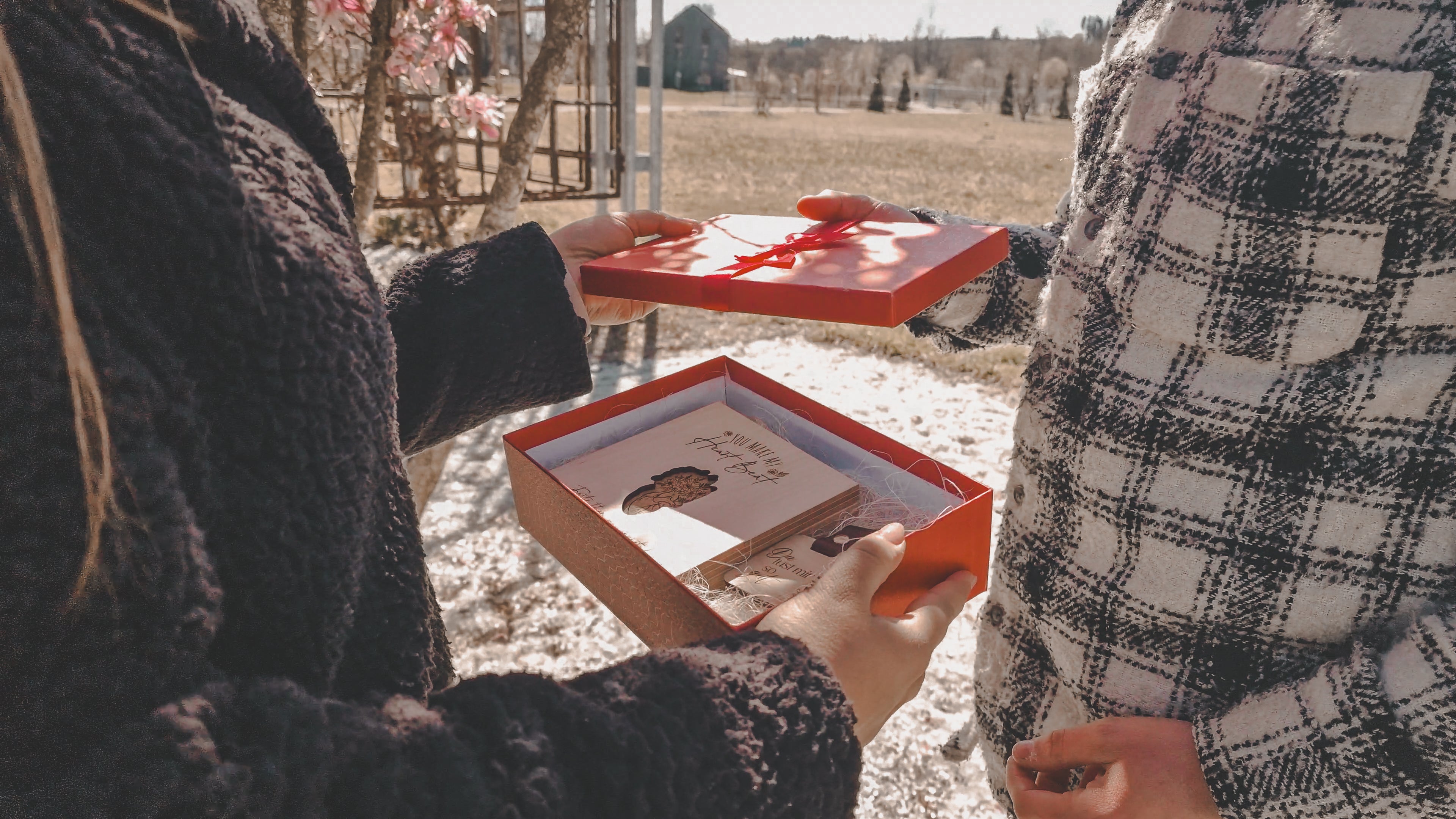 Zwei Personen im Freien: eine überreicht der anderen eine geöffnete rote Geschenkbox mit einem personalisierten Geschenk