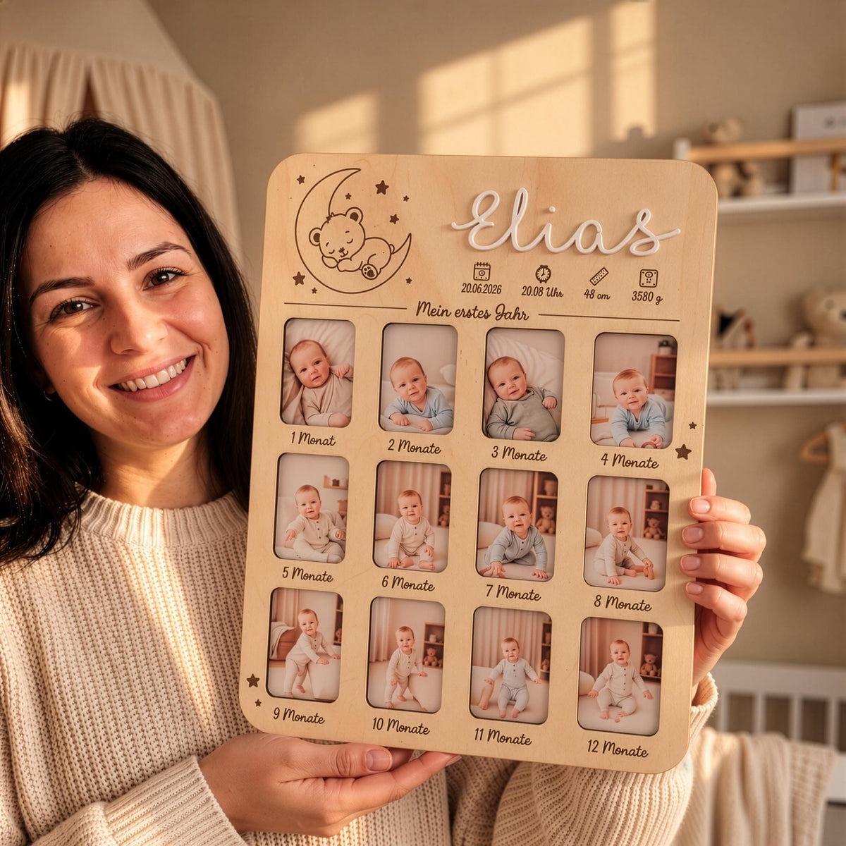 Eine Frau hält eine personalisierte hölzerne Meilensteintafel für Babys erstes Jahr mit zwölf runden Fotorahmen, dem Namen Elias und Geburtsdaten in die Kamera.