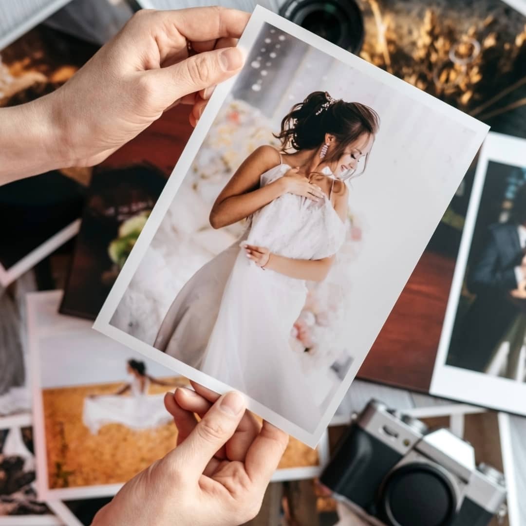 Personalisierbare Fotogeschenke: Hände halten ein ausgedrucktes Foto über einem Stapel Fotos und einer Fotokamera